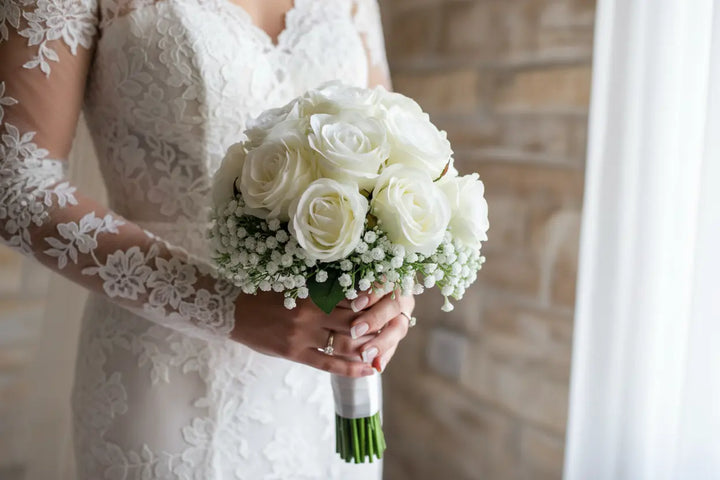 Bride holding a bouquet of white roses in a softly lit room.