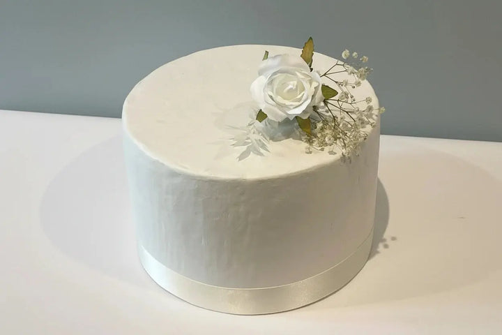 White cake with a single white rose and baby's breath on a gray background